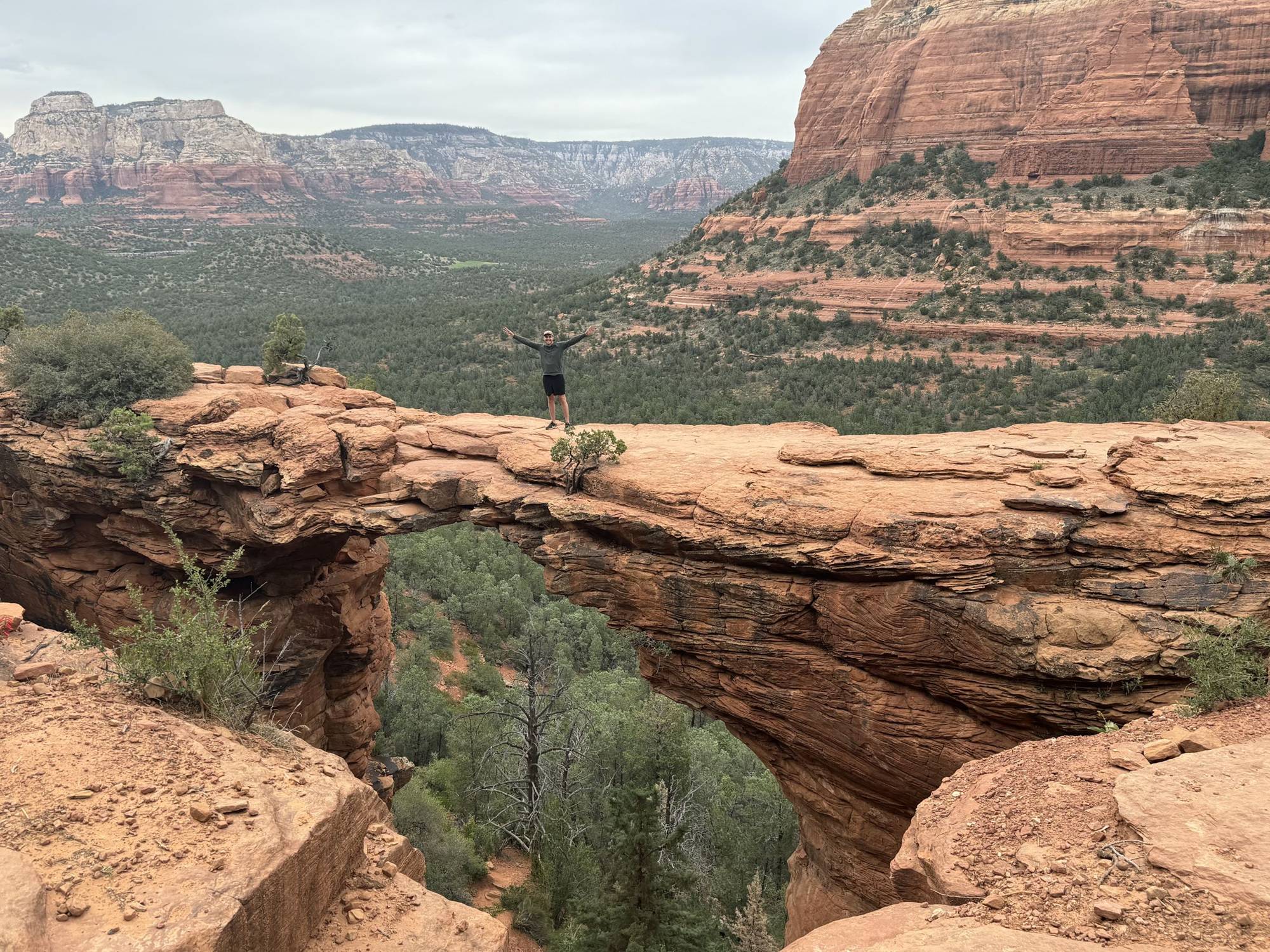 A person standing with arms raised on top of Devil’s Bridge, a natural sandstone arch near Sedona, Arizona